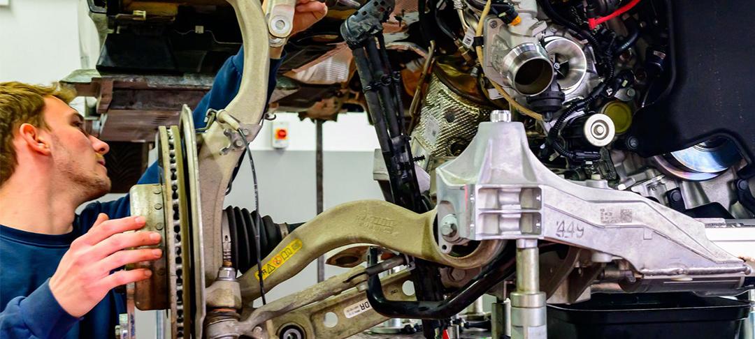 BMW Rhein Ausbildung Karosseriebauer Mechaniker bei der Arbeit an der Vorderachse eines aufgebockten BMW in der Werkstatt.