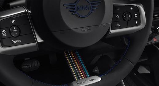 Detailansicht des Multifunktionslenkrads der MINI Paul Smith Edition mit einer vertikalen Stoffspeiche im bunten Signature-Streifendesign und Paul Smith Schriftzug.