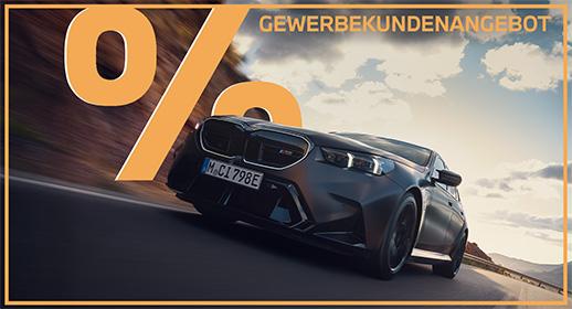  Das Bild zeigt eine dunkle BMW M5 Limousine, die auf einer kurvigen Straße fährt. Im oberen Teil steht der Text „GEWERBEKUNDENANGEBOT“ und links ist ein großes, oranges Prozentsymbol zu sehen. Ein orangefarbener Rahmen umgibt das gesamte Bild.