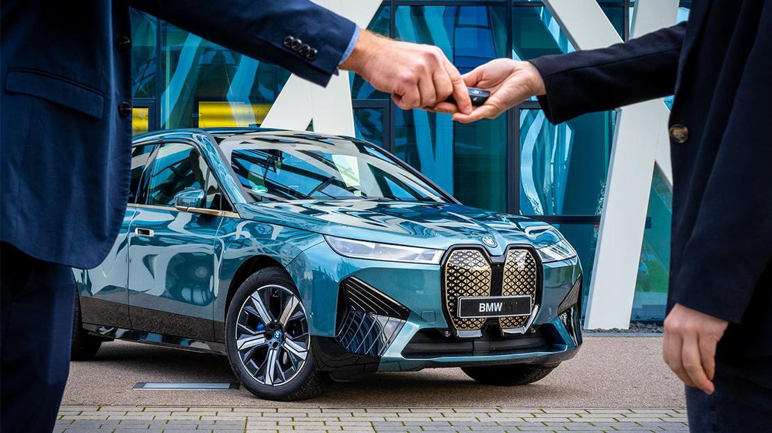 Hände übergeben Autoschlüssel vor einem türkisfarbenen BMW iX.