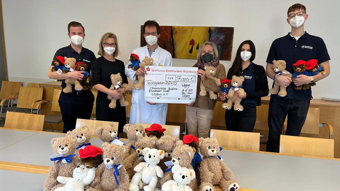 Eine Gruppe von Personen, darunter Mitarbeiter der Rhein Gruppe, überreicht einen Spendenscheck über 7.000 € und Teddybären an "Würzburg hilft e.V.".