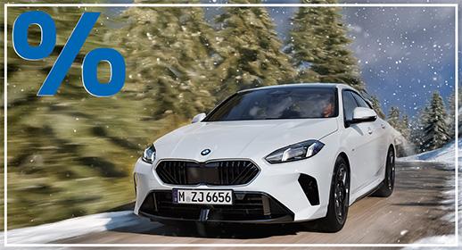 Ein weißes viertüriges BMW 2er Gran Coupé ist von vorne auf einer verschneiten Landstraße zu sehen. Die Fahrt führt durch einen verschneiten Wald. Das Licht ist hell und das Bild wirkt sehr klar. Das blaue Prozentzeichen (%) füllt die obere linke Ecke und signalisieren einen Rabatt oder eine spezielle Finanzierung.  