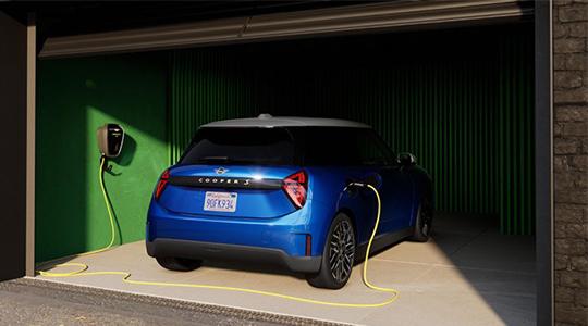 Bild illustriert das Laden zu Hause mithilfe der kompakten MINI Wallbox. Diese fest installierte Ladestation ermöglicht ein deutlich schnelleres und sichereres Aufladen als eine herkömmliche Haushaltssteckdose, sodass das Fahrzeug, wie hier in einer Garage, bequem über Nacht vollständig geladen werden kann. Über die MINI App lässt sich der Ladevorgang zudem intelligent steuern, um beispielsweise bevorzugt eigenen Solarstrom oder günstigere Nachttarife zu nutzen.