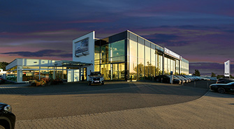 Modernes BMW Rhein Autohaus bei Dämmerung mit beleuchteten Schaufenstern und geparkten BMWs  