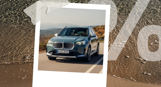 Ein Polaroid-Foto auf Strand-Hintergrund zeigt einen silber-grünen BMW iX1 auf einer Straße. Rechts ist wieder das große, transparente Prozentzeichen (%) zu sehen.